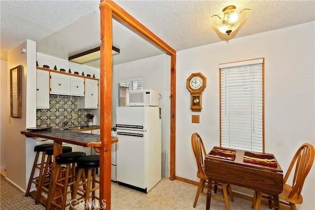 kitchen with backsplash, a textured ceiling, white appliances, beamed ceiling, and white cabinets