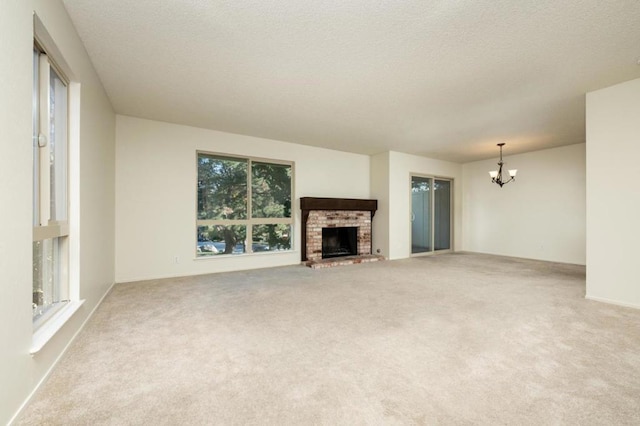 unfurnished living room featuring a brick fireplace, a notable chandelier, a wealth of natural light, and carpet flooring