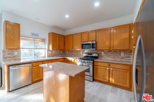 kitchen featuring sink, a center island, light stone counters, appliances with stainless steel finishes, and light wood-type flooring