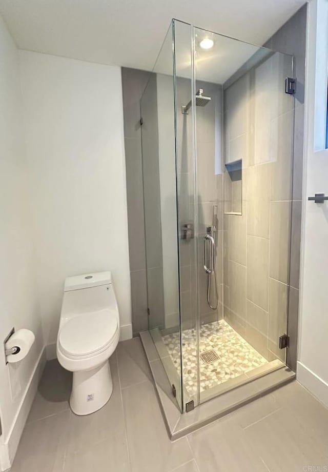 bathroom with tile patterned floors, a shower stall, toilet, and baseboards