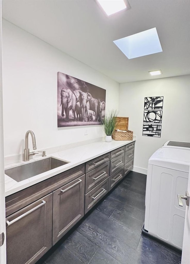 laundry room featuring dark wood finished floors, a skylight, cabinet space, separate washer and dryer, and a sink