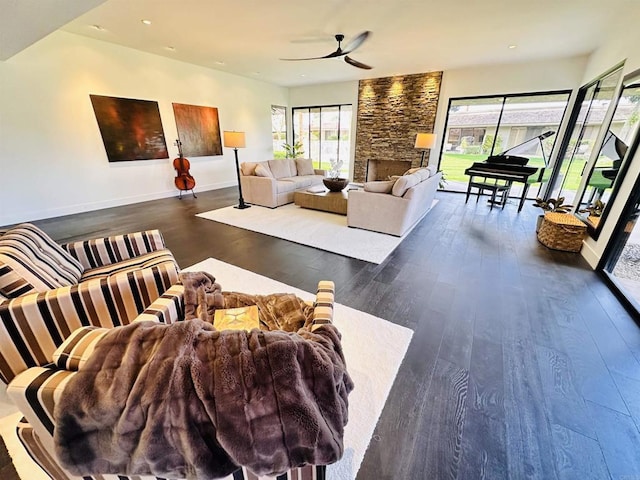 living area with dark wood-style floors, recessed lighting, a stone fireplace, baseboards, and ceiling fan