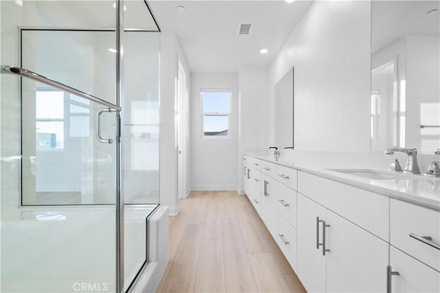 bathroom with a shower with shower door, hardwood / wood-style floors, and vanity