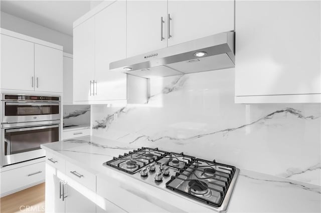 kitchen with light stone counters, white cabinets, gas cooktop, and stainless steel double oven