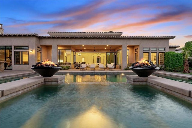 back house at dusk with ceiling fan, an outdoor fire pit, and a patio