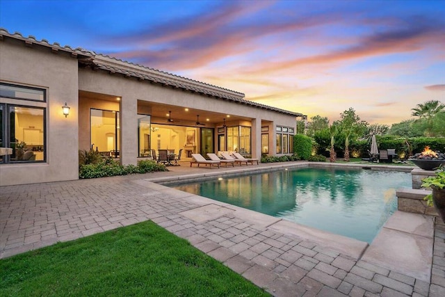 pool at dusk with ceiling fan and a patio