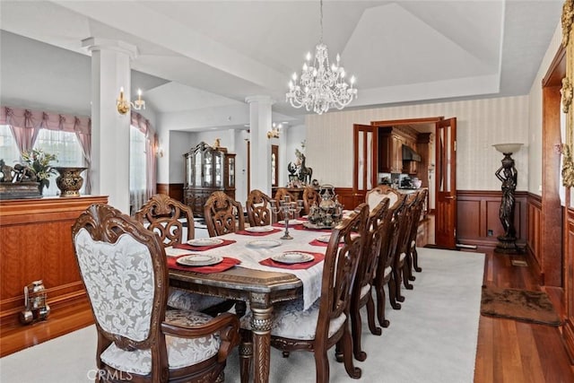 dining space with ornate columns, wood-type flooring, vaulted ceiling, and a notable chandelier