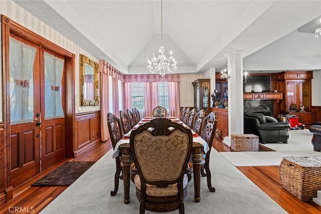 dining space featuring french doors, a notable chandelier, decorative columns, lofted ceiling, and hardwood / wood-style flooring