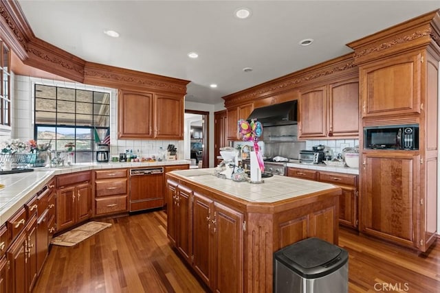 kitchen with dishwasher, wall chimney range hood, tile counters, a kitchen island, and black microwave