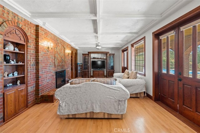 living room with light wood-type flooring, a fireplace, brick wall, and coffered ceiling