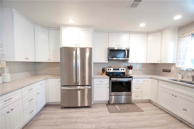 kitchen featuring light stone countertops, stainless steel appliances, sink, white cabinets, and light hardwood / wood-style floors