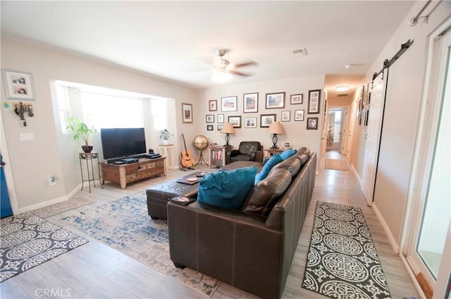 living room featuring a barn door, ceiling fan, and light wood-type flooring