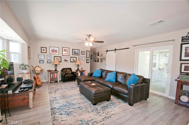 living room featuring a barn door, ceiling fan, and light hardwood / wood-style floors