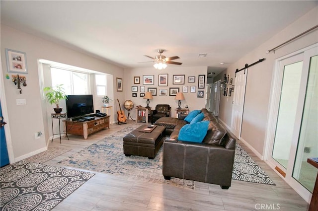 living room featuring ceiling fan, a barn door, and light hardwood / wood-style floors