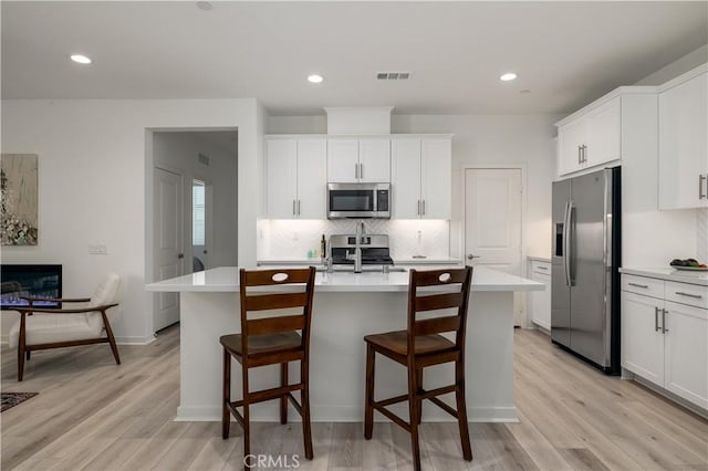 32879 Brunello Way, Temecula, CA 92591 - kitchen featuring stainless steel appliances, light countertops, a kitchen island with sink, backsplash, and light wood-style floors