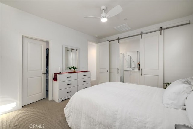 bedroom with light carpet, ceiling fan, ensuite bathroom, and a barn door