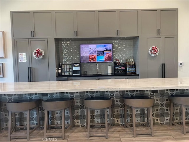 bar with decorative backsplash, light stone countertops, and gray cabinets