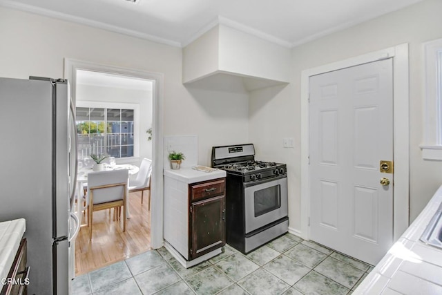 kitchen featuring tile counters, light tile patterned floors, appliances with stainless steel finishes, and ornamental molding