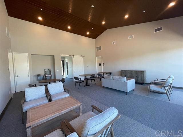 living room with a barn door, carpet floors, and high vaulted ceiling