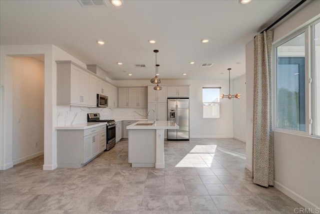 kitchen with sink, tasteful backsplash, decorative light fixtures, a kitchen island with sink, and appliances with stainless steel finishes