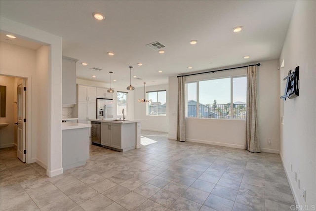 kitchen featuring plenty of natural light, white fridge with ice dispenser, hanging light fixtures, and a kitchen island with sink