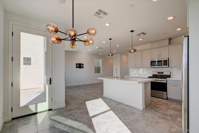 kitchen with decorative backsplash, appliances with stainless steel finishes, a kitchen island with sink, a chandelier, and hanging light fixtures