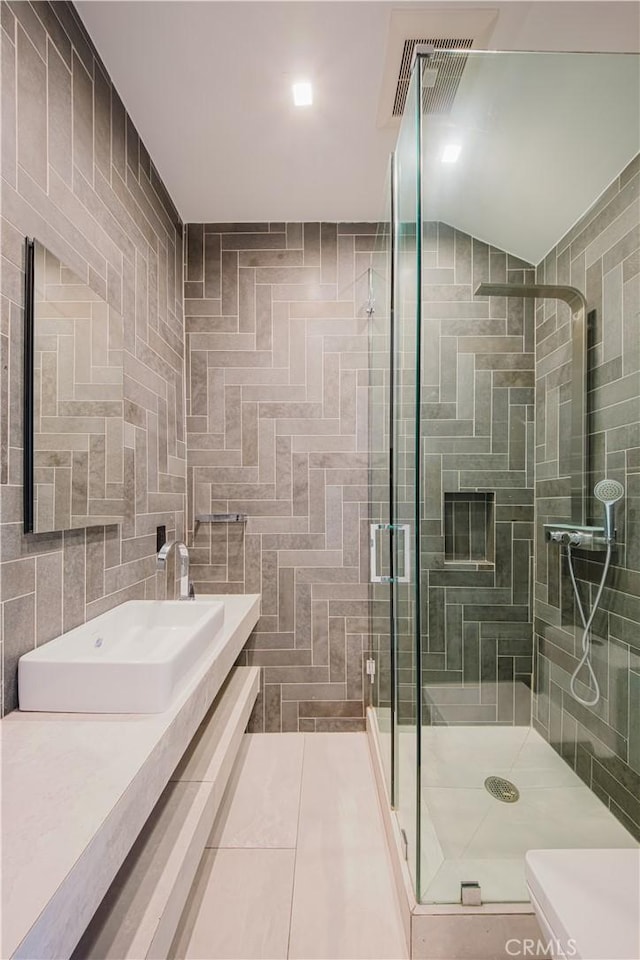 bathroom with tile patterned floors, vanity, vaulted ceiling, tile walls, and a shower with shower door