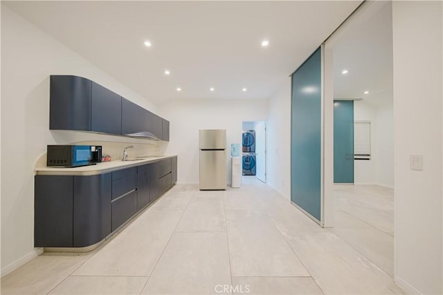 kitchen with light tile patterned flooring, stainless steel refrigerator, stacked washer and clothes dryer, and sink