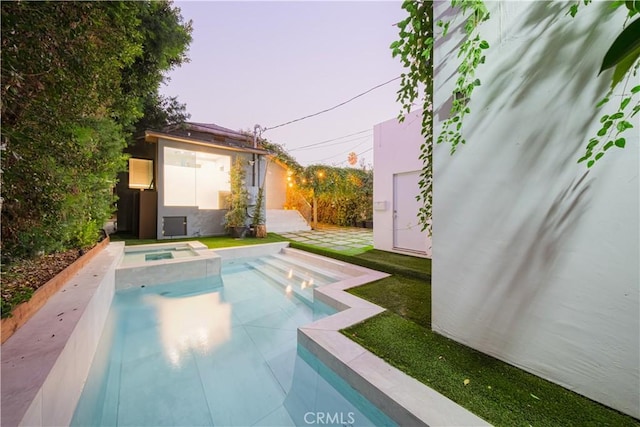 pool at dusk with an in ground hot tub and a patio