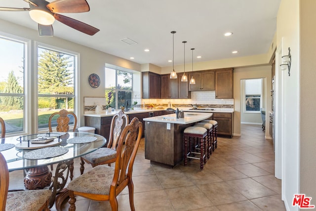 kitchen featuring tasteful backsplash, a kitchen island with sink, ceiling fan, hanging light fixtures, and a breakfast bar area