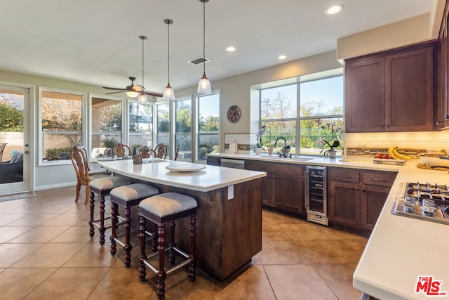 kitchen featuring ceiling fan, beverage cooler, an island with sink, decorative light fixtures, and decorative backsplash