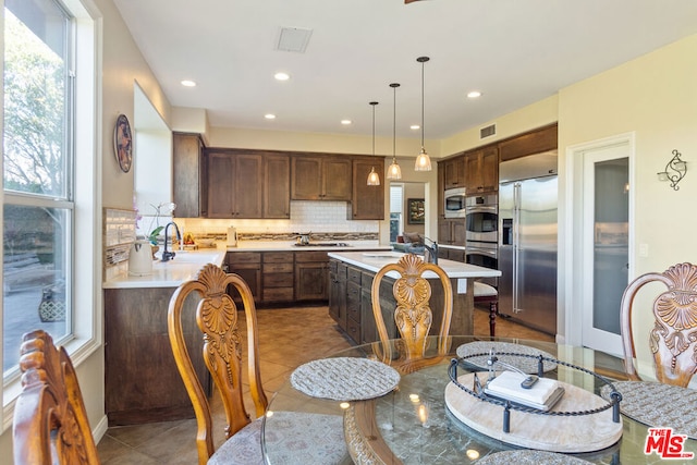 kitchen featuring plenty of natural light, decorative backsplash, stainless steel appliances, and decorative light fixtures