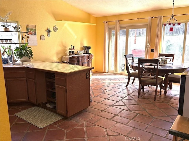 kitchen with tile countertops, vaulted ceiling, hanging light fixtures, and a textured ceiling