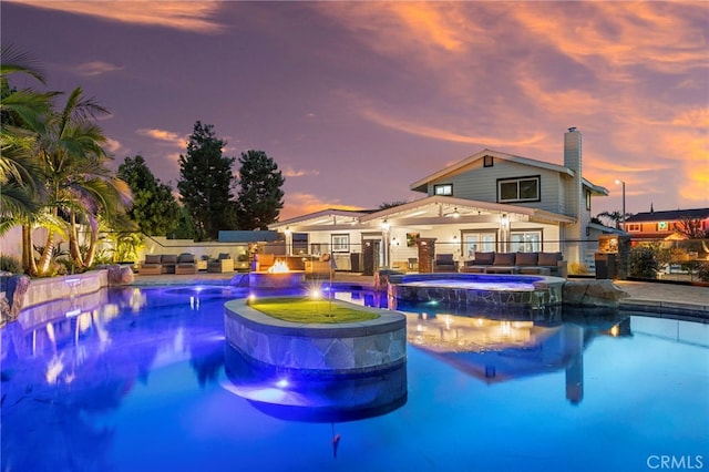 pool at dusk with an in ground hot tub, a patio area, and pool water feature