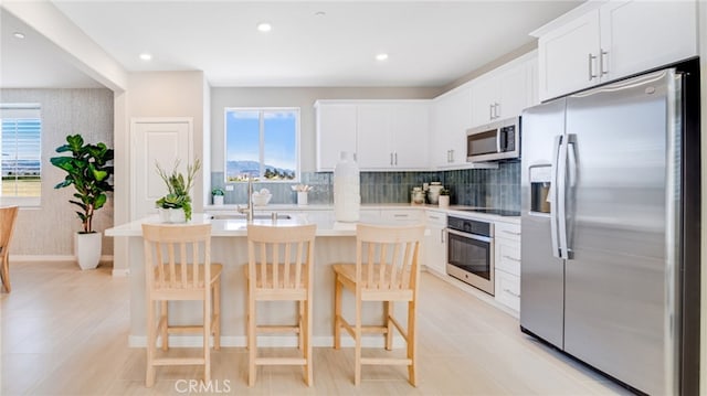 kitchen featuring white cabinetry, tasteful backsplash, an island with sink, a breakfast bar area, and appliances with stainless steel finishes