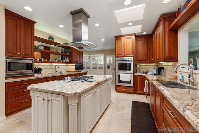 kitchen with island exhaust hood, appliances with stainless steel finishes, a skylight, sink, and a kitchen island