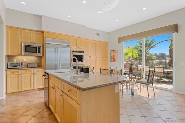 kitchen featuring light brown cabinetry, a kitchen island with sink, sink, light tile patterned floors, and built in appliances