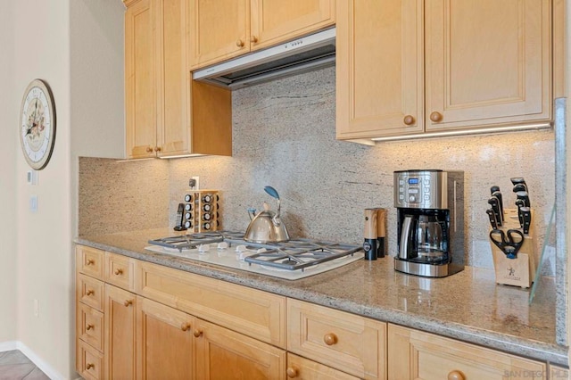 kitchen featuring light brown cabinets, light stone counters, white gas cooktop, and backsplash