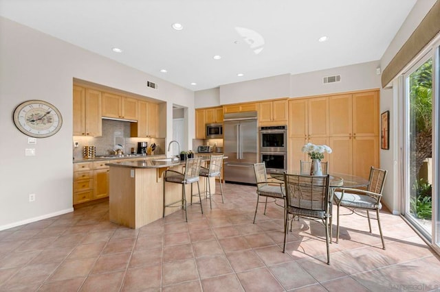 kitchen featuring stainless steel appliances, a kitchen breakfast bar, tasteful backsplash, an island with sink, and light tile patterned flooring