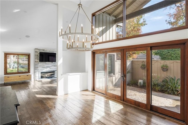 doorway with wood-type flooring, high vaulted ceiling, an inviting chandelier, and a stone fireplace