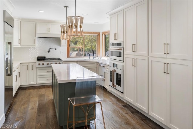 kitchen with appliances with stainless steel finishes, dark hardwood / wood-style flooring, tasteful backsplash, a kitchen island, and white cabinetry