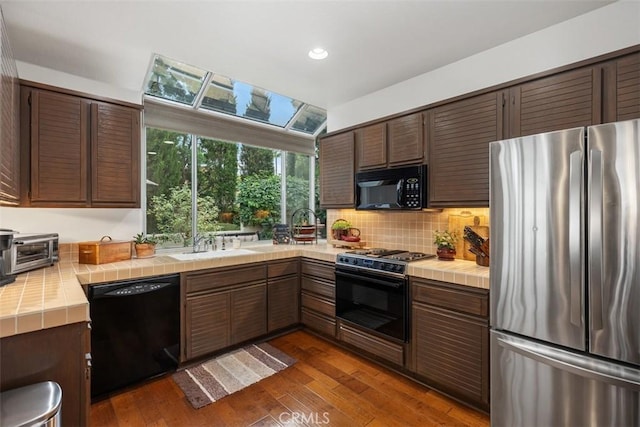 kitchen featuring sink, dark hardwood / wood-style floors, backsplash, tile countertops, and black appliances