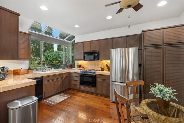 kitchen with a skylight, ceiling fan, black appliances, dark hardwood / wood-style floors, and tile counters