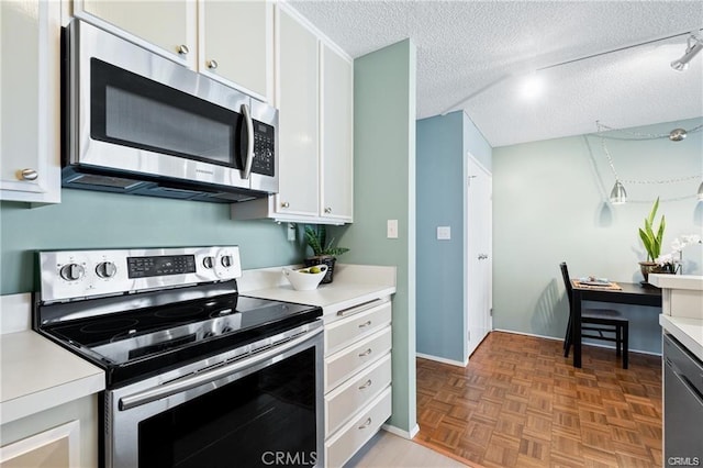 kitchen with dark parquet flooring, white cabinetry, a textured ceiling, and appliances with stainless steel finishes