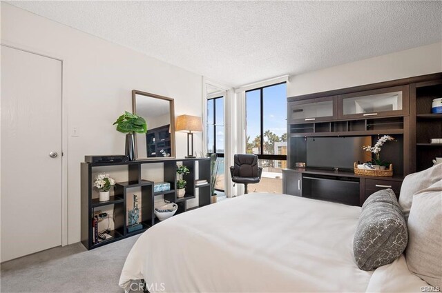 bedroom featuring a textured ceiling, light colored carpet, and a wall of windows