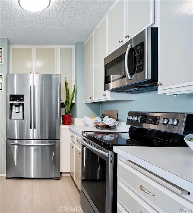 kitchen with a textured ceiling, light hardwood / wood-style floors, white cabinetry, and stainless steel appliances