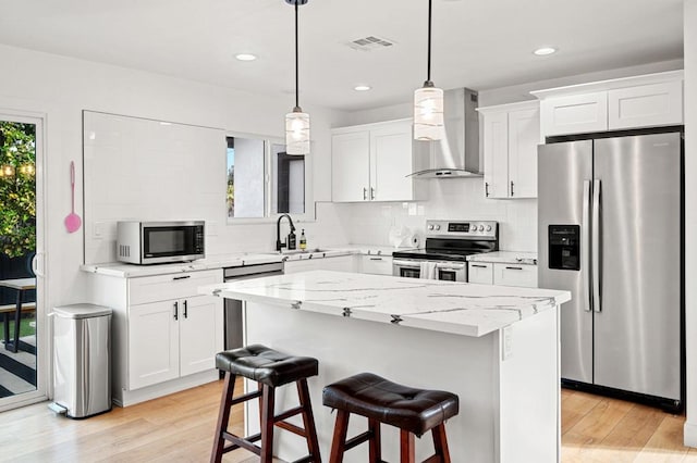 kitchen with stainless steel appliances, wall chimney exhaust hood, white cabinetry, and decorative light fixtures