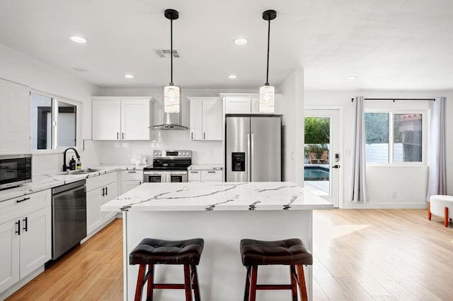 kitchen featuring a center island, sink, stainless steel appliances, white cabinets, and wall chimney exhaust hood