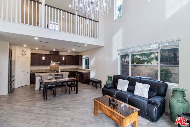 living room with a towering ceiling, a wealth of natural light, a notable chandelier, and light hardwood / wood-style flooring