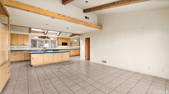 kitchen featuring light brown cabinets, vaulted ceiling with beams, a kitchen island, a fireplace, and light tile patterned flooring